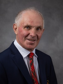 Councilor Jim Palmer wearing a dark blue suit with a red, green and yellow plaid tye, he has short white and light brown hair. 